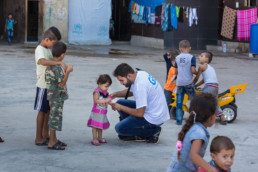 Addullah Nimje (Mitte, Cap Anamur Krankenpfleger) im Gespräch mit einer kleinen Patientin im Innenhof des „Settlement“ Hochhaus in Sidon. Hier leben circa 200 syrische Bürgerkriegs-Flüchtlingfamilien (circa 1.200 Menschen) unter schwierigsten Bedingungen.