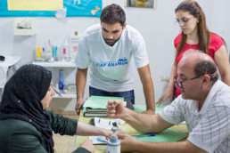 Examination room (from right, Dr. Ousama Dimassi (Healthstation), Healthstation staff member, Addullah Nimje (Cap Anamur nurse) talking to a patient (Syrian civil war refugee) at the Healthstation in Sidon.