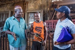 Movie Konneh (centre, former street child) now works successfully in a metal factory. Raymond Tommy (right, social worker) talking to the boss (left). Regular visits and checks consolidate the success of the repatriation programme.