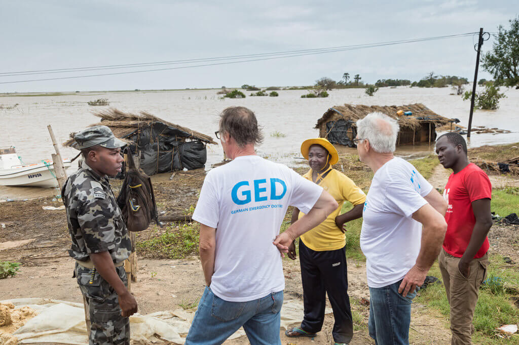 Factfindung eines Cap Anamur Teams (rechts, Lutz Sarzio, Krankenpfeger und Michael Schlüssel, links, Projekt Koordinator) nach der Unwetterkatastrophe in Mosambik – hier in der überfluteten Region Tica im Gespräch mit einem Marinesoldaten und Mitarbeitern einer staatlichen Organisation für Katastrophenschutz.